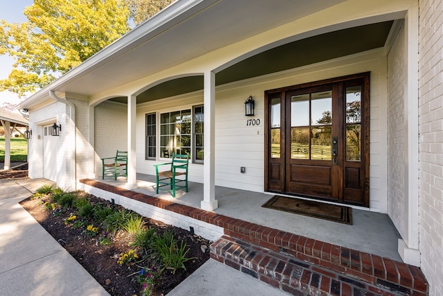 entrance to property featuring a garage, covered porch, and brick siding