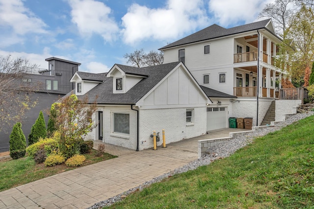 back of property featuring a balcony, a garage, and a lawn