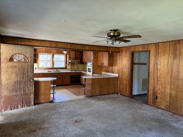 kitchen featuring sink, tasteful backsplash, white oven, kitchen peninsula, and light carpet