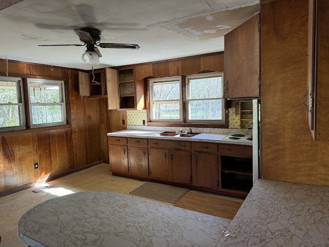 kitchen featuring ceiling fan, sink, wooden walls, decorative backsplash, and light wood-type flooring