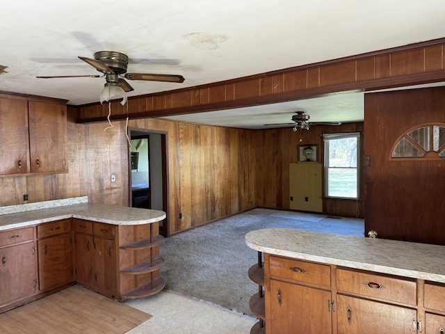 kitchen with kitchen peninsula, wooden walls, ceiling fan, and light carpet