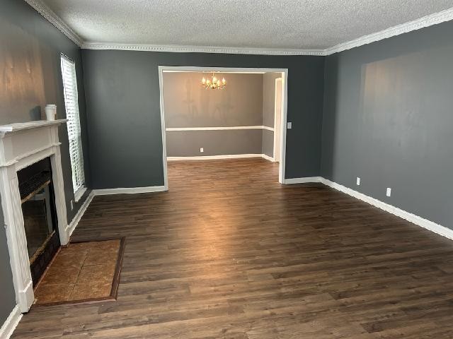 unfurnished living room with a chandelier, ornamental molding, a textured ceiling, and dark wood-type flooring