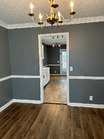 unfurnished dining area with a textured ceiling, a notable chandelier, ornamental molding, and dark wood-type flooring