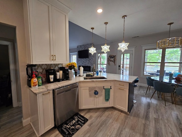 kitchen featuring kitchen peninsula, white cabinetry, a stone fireplace, and stainless steel dishwasher