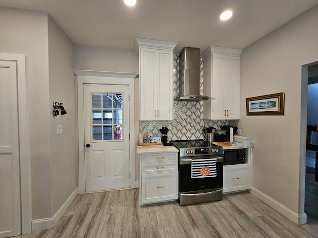 kitchen with black microwave, white cabinetry, wall chimney exhaust hood, light hardwood / wood-style flooring, and stainless steel electric stove