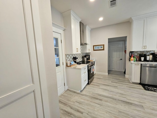 kitchen featuring decorative backsplash, appliances with stainless steel finishes, wall chimney exhaust hood, white cabinets, and light hardwood / wood-style floors