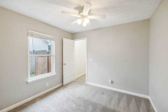 empty room with ceiling fan, light colored carpet, and a textured ceiling