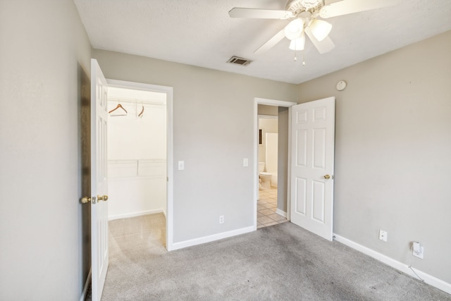 unfurnished bedroom with a walk in closet, ceiling fan, a closet, and light carpet