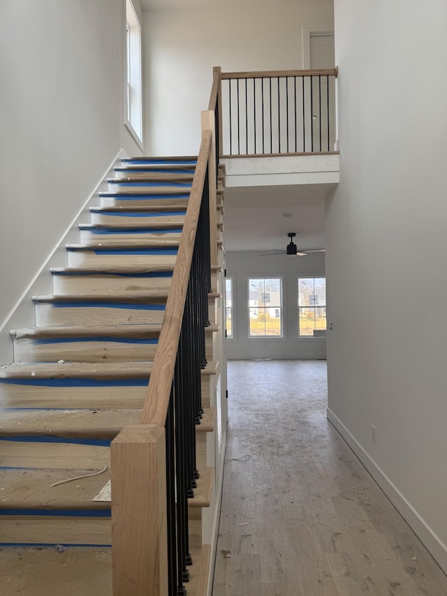 stairway with ceiling fan, wood-type flooring, and a high ceiling