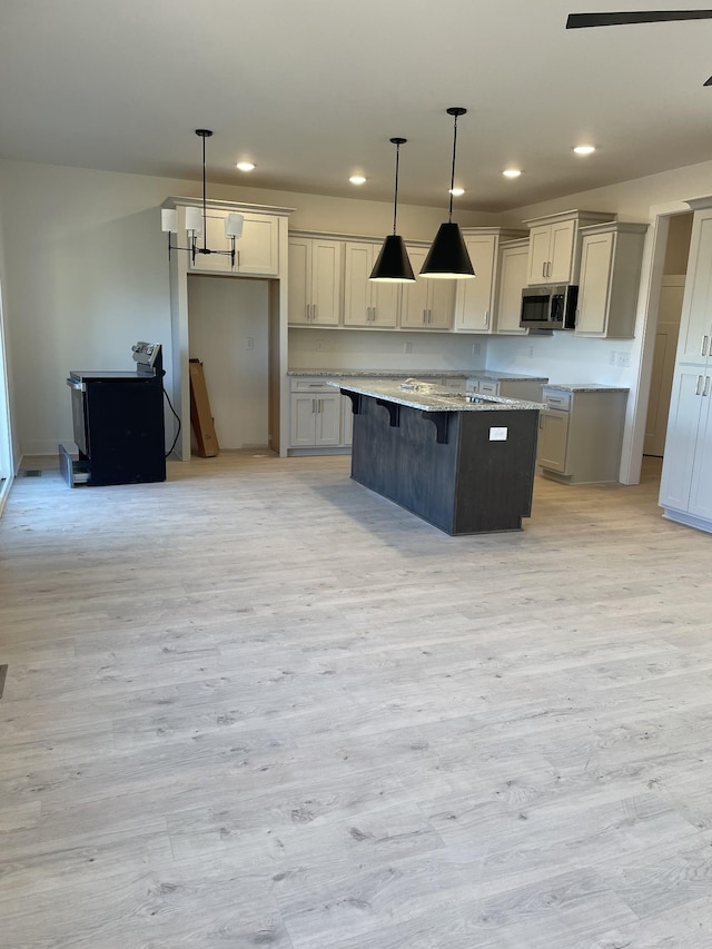 kitchen with a kitchen island, a kitchen bar, hanging light fixtures, light stone counters, and light hardwood / wood-style floors