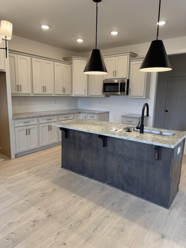 kitchen featuring gray cabinets, hanging light fixtures, light stone counters, and light hardwood / wood-style flooring