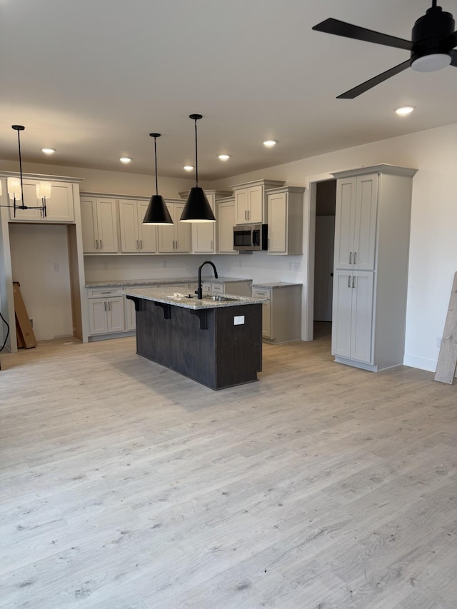 kitchen with gray cabinets, an island with sink, pendant lighting, and light stone countertops