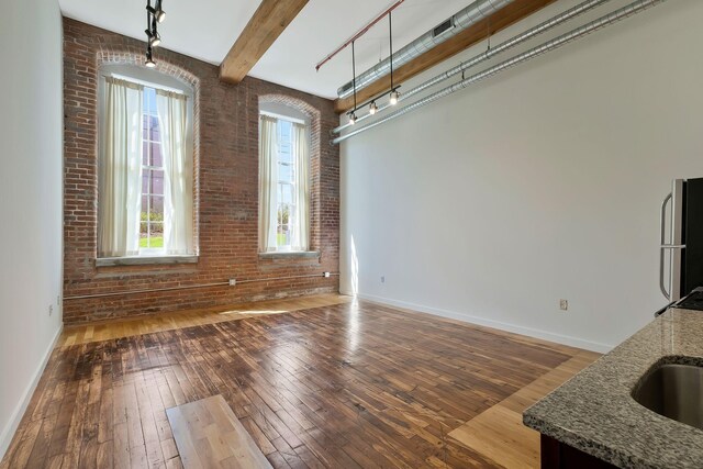 unfurnished dining area featuring healthy amount of natural light, hardwood / wood-style flooring, baseboards, beamed ceiling, and brick wall