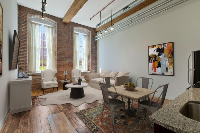 dining area featuring healthy amount of natural light, hardwood / wood-style flooring, brick wall, baseboards, and rail lighting