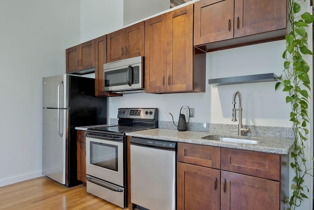 kitchen with stainless steel appliances, a sink, light wood-style flooring, light stone countertops, and open shelves