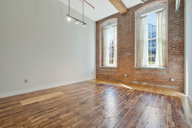 spare room with wood-type flooring, beam ceiling, baseboards, and brick wall