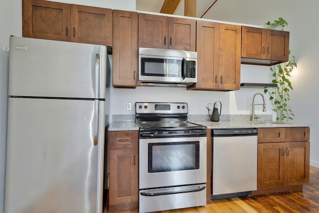 kitchen with appliances with stainless steel finishes, open shelves, a sink, wood finished floors, and light stone countertops