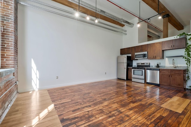 kitchen with appliances with stainless steel finishes, track lighting, dark wood-style floors, beamed ceiling, and a towering ceiling