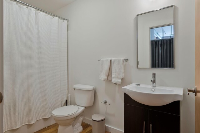 bathroom with toilet, wood finished floors, vanity, baseboards, and shower / bath combo with shower curtain