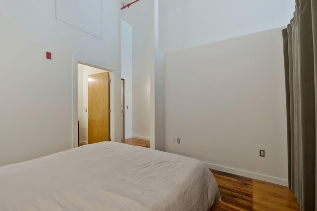 bedroom with wood finished floors, baseboards, and a high ceiling