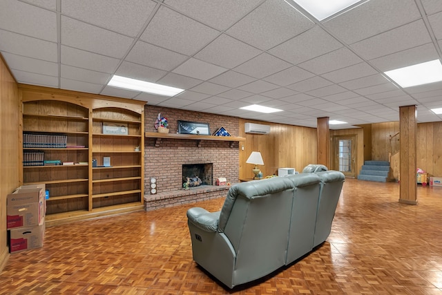 living room with wooden walls, a fireplace, a drop ceiling, and a wall mounted air conditioner