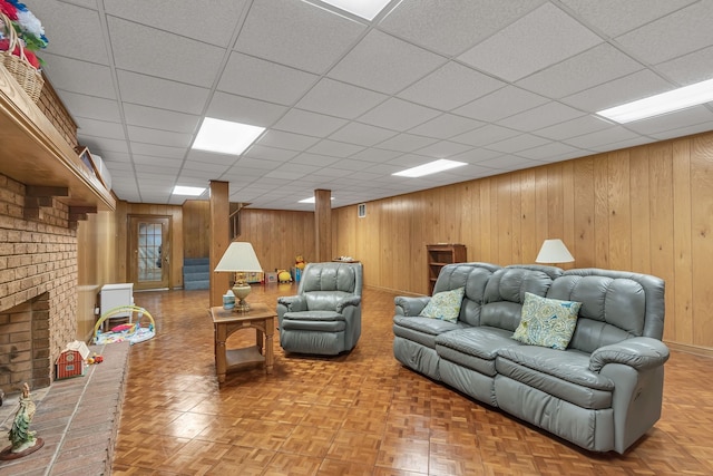 living room featuring a paneled ceiling, a brick fireplace, and wood walls