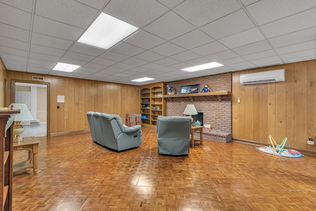 living room with a wall mounted air conditioner, a drop ceiling, a fireplace, and wood walls