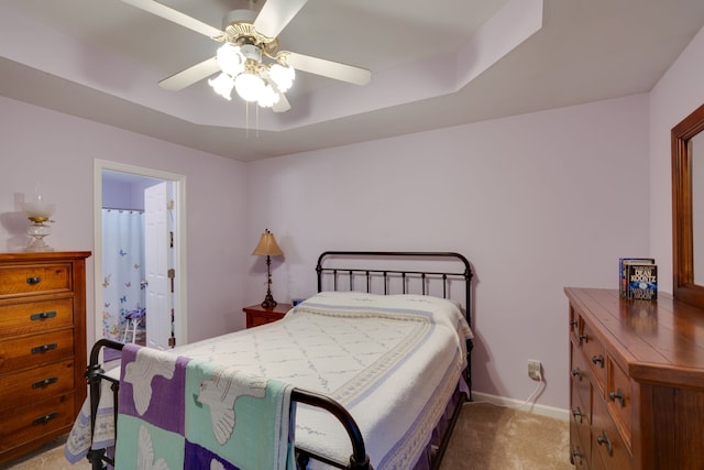 carpeted bedroom with connected bathroom, a raised ceiling, and ceiling fan