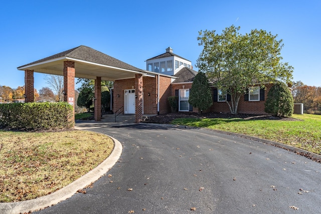 view of front of house with a front lawn, a carport, and central AC unit