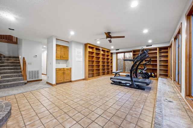 exercise room featuring ceiling fan, light tile patterned floors, and a textured ceiling