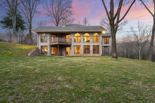 back house at dusk with a yard and a balcony