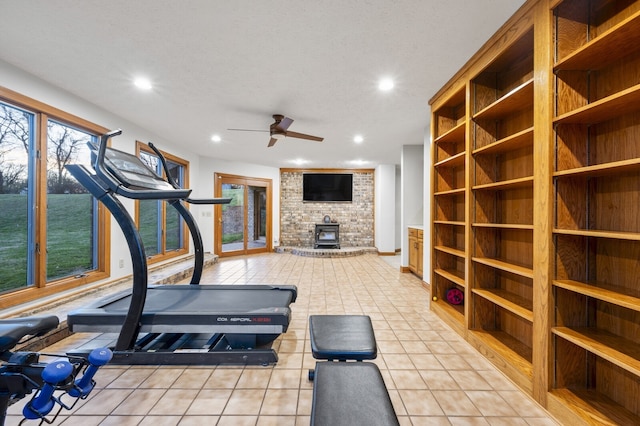 workout room featuring ceiling fan, a wood stove, a textured ceiling, and light tile patterned floors