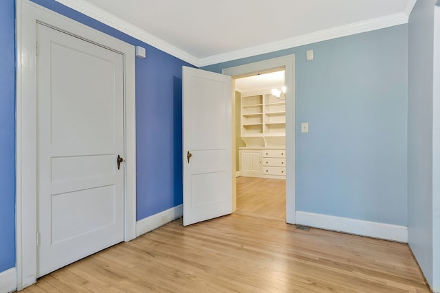 unfurnished bedroom featuring a spacious closet, a closet, ornamental molding, and light hardwood / wood-style flooring