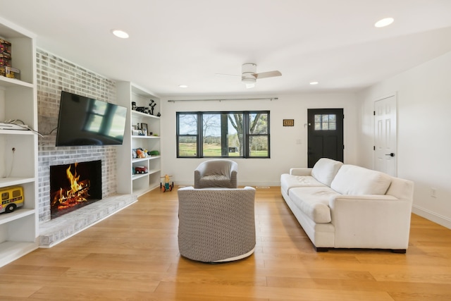 living room with a brick fireplace, ceiling fan, and light wood-type flooring