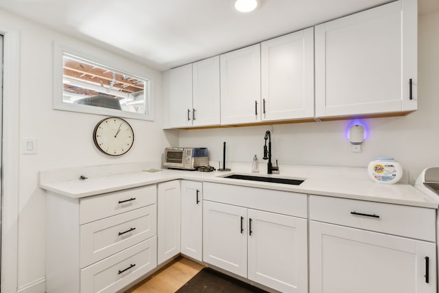 kitchen with light stone countertops, light wood-type flooring, white cabinetry, and sink