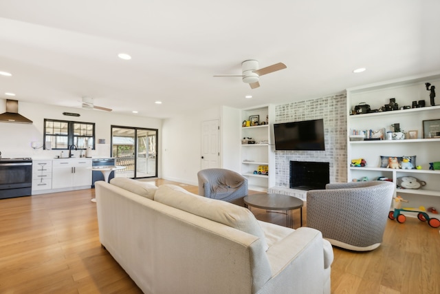 living room featuring a fireplace, light hardwood / wood-style floors, ceiling fan, and sink