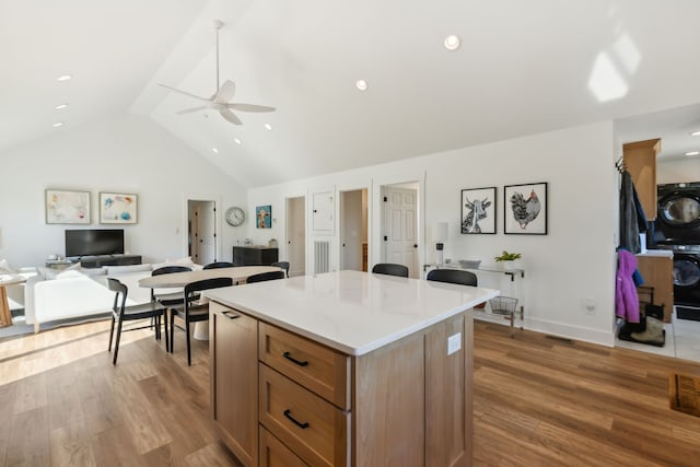 kitchen with ceiling fan, a kitchen island, stacked washing maching and dryer, and light hardwood / wood-style flooring