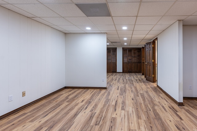 spare room with a paneled ceiling, light hardwood / wood-style floors, and wooden walls