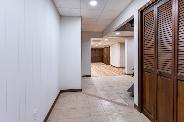 corridor featuring wood walls, a drop ceiling, and light tile patterned flooring