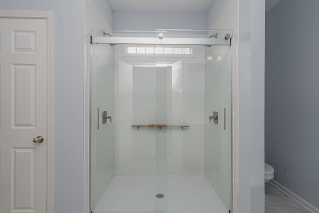 bathroom featuring a shower with shower door and toilet