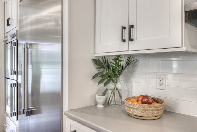 interior details with backsplash, white cabinetry, and high end fridge