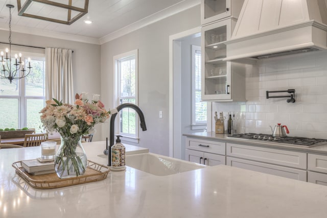 kitchen with white cabinets, sink, decorative light fixtures, custom range hood, and stainless steel gas cooktop