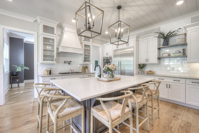 kitchen with white cabinets, decorative light fixtures, stainless steel appliances, and an island with sink