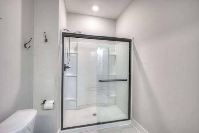 bathroom featuring tile patterned flooring, toilet, and a shower with shower door