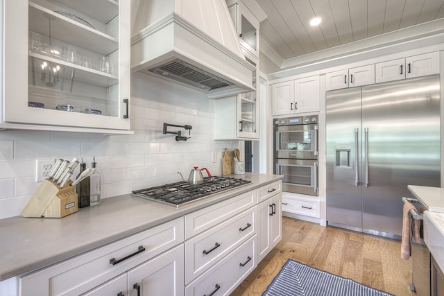 kitchen featuring white cabinetry, stainless steel appliances, decorative backsplash, custom range hood, and light wood-type flooring