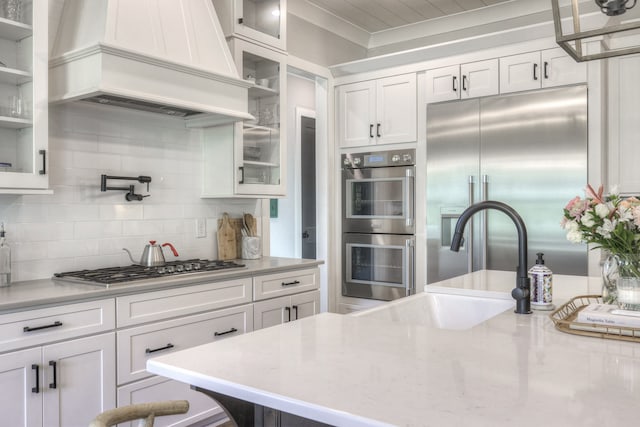 kitchen featuring backsplash, premium range hood, sink, appliances with stainless steel finishes, and white cabinetry