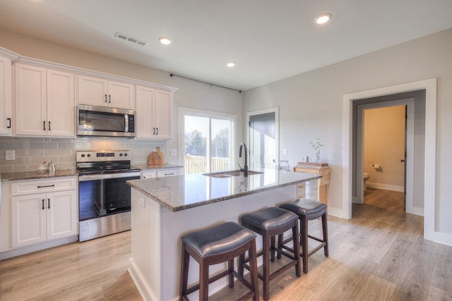 kitchen with a center island with sink, white cabinets, light hardwood / wood-style flooring, and appliances with stainless steel finishes