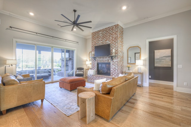 living room featuring light wood-type flooring, a brick fireplace, ceiling fan, and crown molding