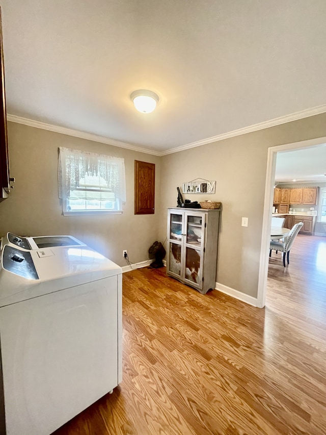 clothes washing area featuring a wealth of natural light, washer and dryer, light hardwood / wood-style floors, and ornamental molding