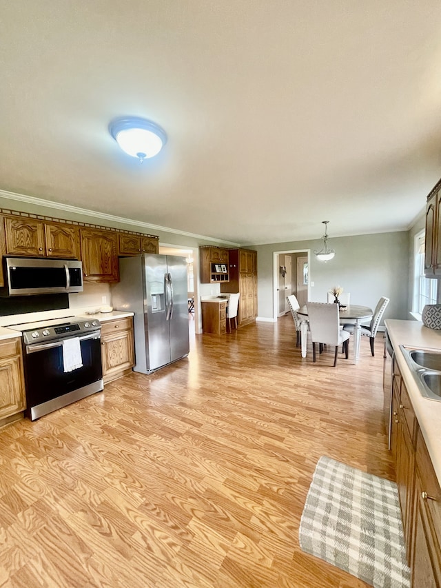 kitchen featuring sink, light hardwood / wood-style flooring, ornamental molding, appliances with stainless steel finishes, and decorative light fixtures